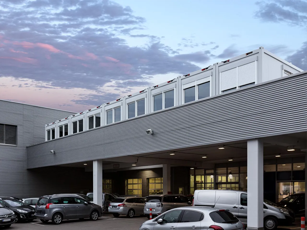 foto von einem autohaus in wien, welches eine containeranlage auf dem parkdeck oberhalb des eingangs hat aus neun bürocontainern.