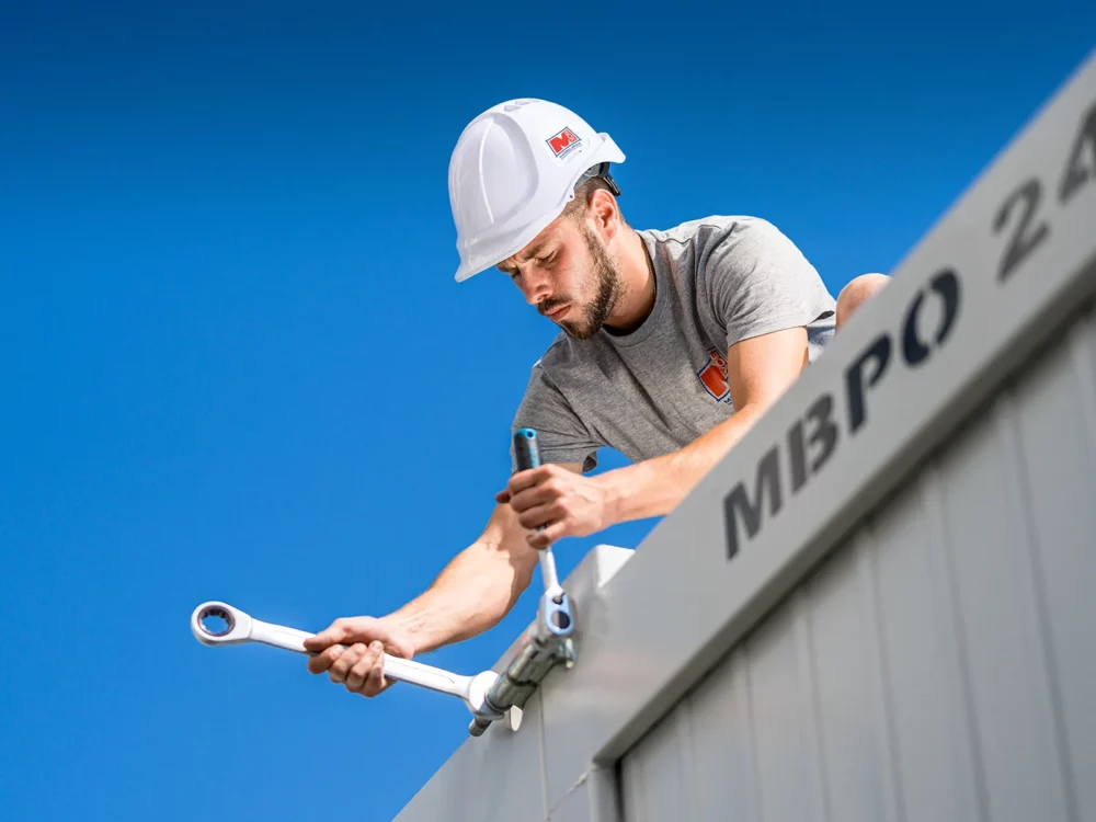 containermonteur von mobilbox wie er mit werkzeug zwei container zusammenzieht.