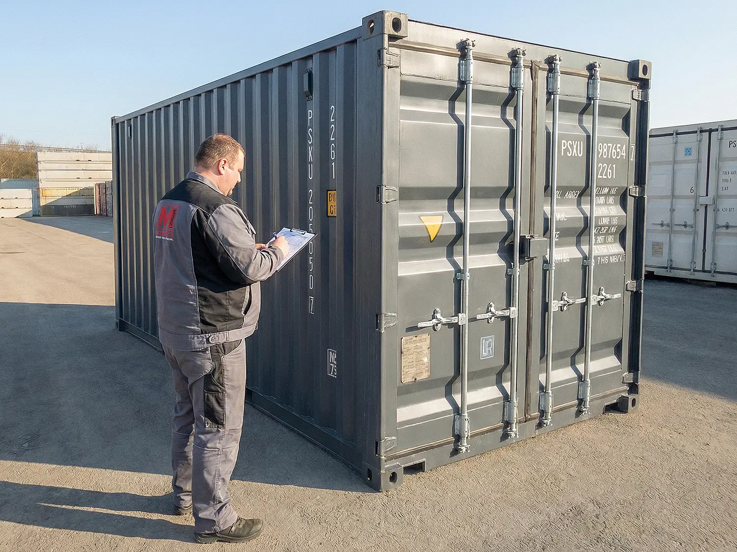Depotmitarbeiter wie dieser mit einem Klemmbrett den Zustand eines gebrauchten Seecontainers dokumentiert und sichtet.